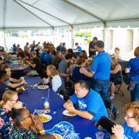 A wide shot of the gvsu party that is held right outside the stadium. Mostly everyone is seated and enjoying their food.